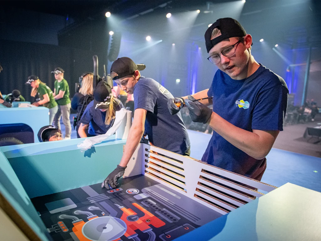 Deltagare i Yrkeskampen byter olja i en personbils-attrapp